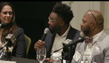 Two men and a woman speaking at a table