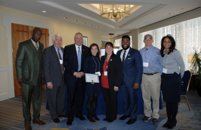 Members of the Institute for Municipal and Regional Policy standing while a member fourth from the left holds a paper award.